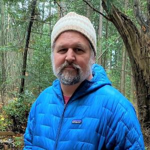 bearded man in blue puffy coat and white hat outside
