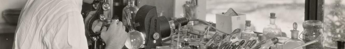 Black and white photo of man operating microscope on lab desk